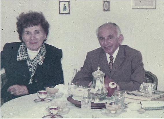 Kurt and Hanna Loewenstein seated at a laid table set with coffee and cake, both smiling.